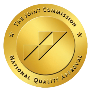A gold circular seal with the text "The Joint Commission National Quality Approval" surrounding a geometric logo in the center, representing excellence in addiction treatment in Philadelphia PA.