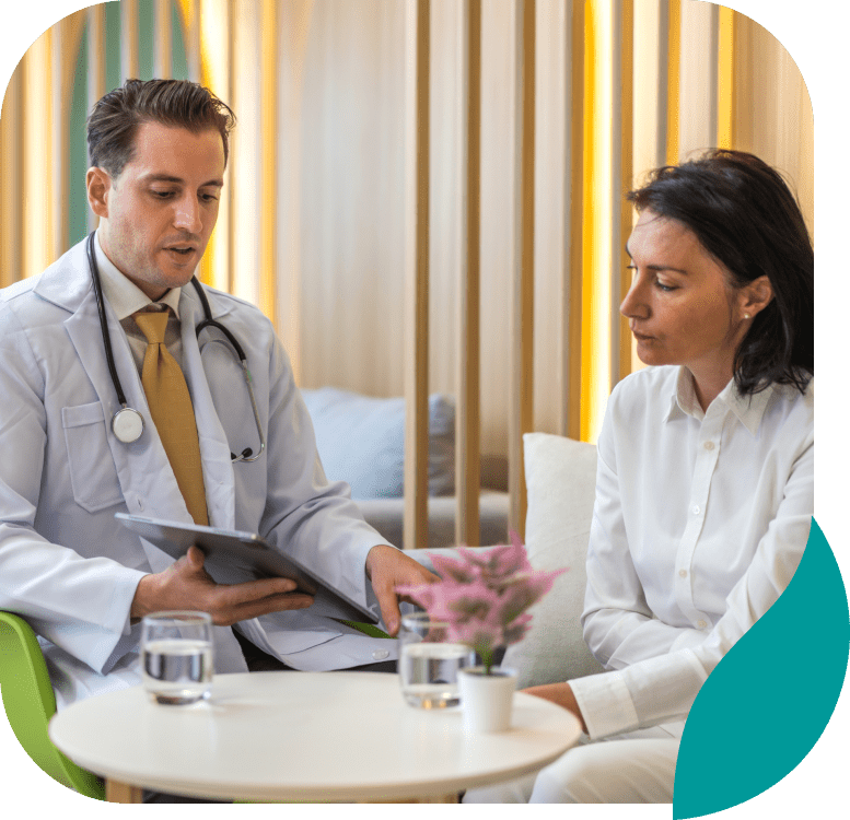 A male doctor with a stethoscope shows a tablet to a woman beside him as they discuss anxiety treatment in Wayne PA in a modern, well-lit office with water glasses and a small plant on the table.