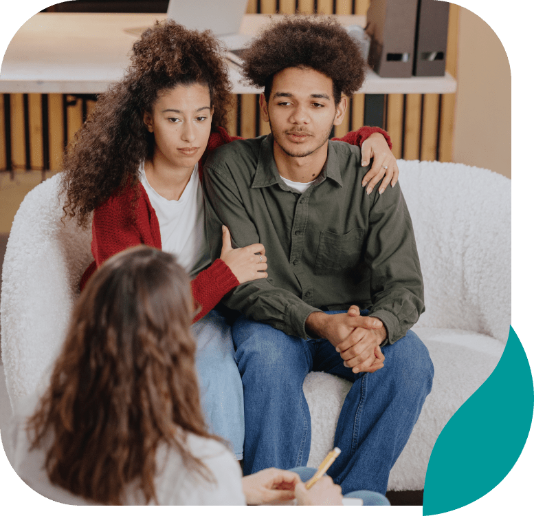 A couple sits closely together on a couch, looking attentive and serious, while a person with long hair, seen from behind, talks to them—suggesting a counseling session focused on depression treatment in Philadelphia PA.