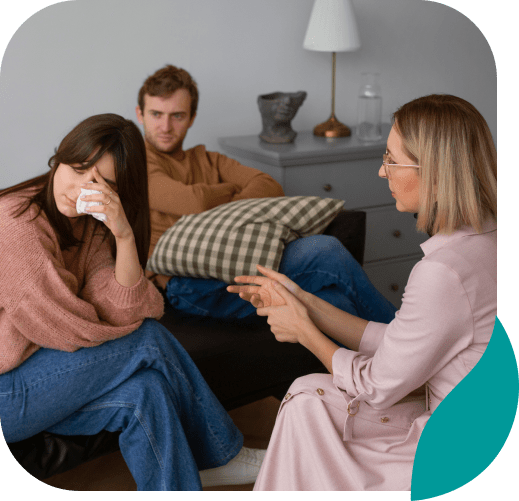 A woman sits on a couch, visibly upset and wiping her face with a tissue. A man sits beside her, looking concerned. Across from them, a therapist discusses options for anxiety treatment in Wayne PA.