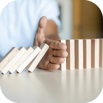 A hand stops a row of falling wooden dominoes, preventing the rest from toppling over, symbolizing intervention or risk management.