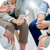 Four people sitting in a circle having a discussion, with only their hands and part of their bodies visible, suggesting a group conversation or support meeting.