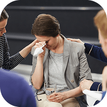 A woman crying while another woman holds a glass of water.