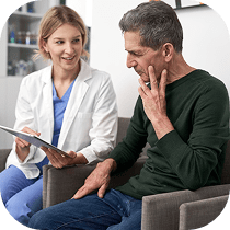 A healthcare professional shows a tablet to an older man who is touching his jaw, possibly discussing his symptoms or medical concerns in a clinical setting.
