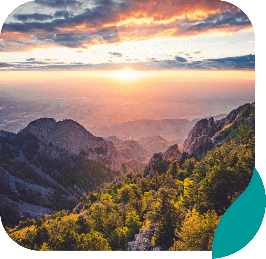 A vibrant sunset over a mountain range, with sunlight illuminating rocky peaks and lush green forests below, under a partly cloudy sky. A rounded graphic element is overlaid in the lower right corner.